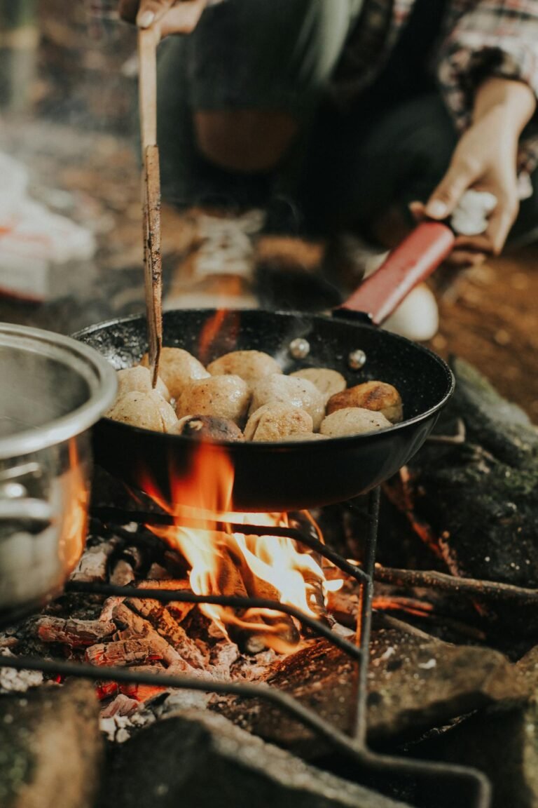 Crop anonymous cook frying potatoes in metal pan on grill standing in nature on stones