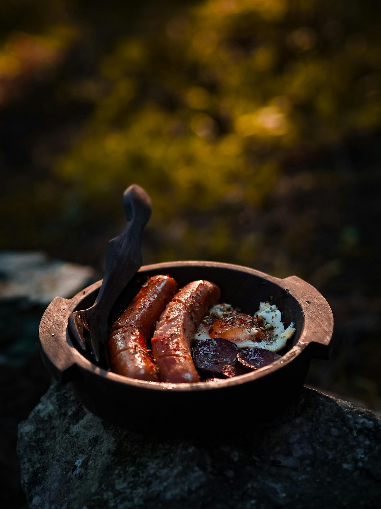 Hearty breakfast with sausages and eggs cooked outdoors in a rustic setting.